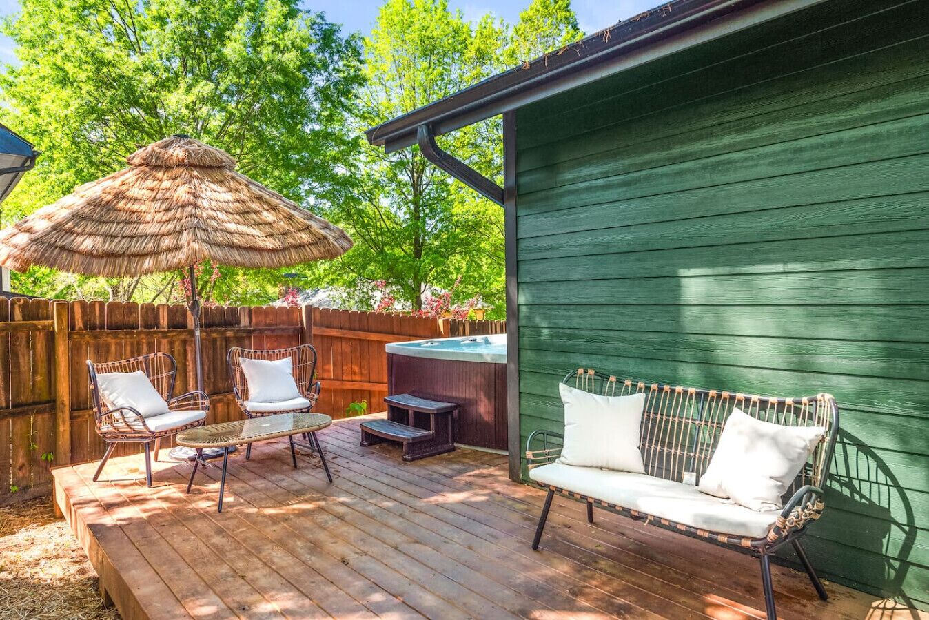 Una terraza de madera con mobiliario exterior, un jacuzzi y un cobertizo verde.