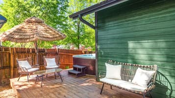 Una terraza de madera con mobiliario exterior, un jacuzzi y un cobertizo verde.