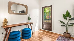Une pièce avec un bureau en bois, des poufs bleus, un miroir et une porte donnant sur un jardin.