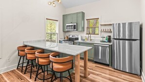 Une cuisine moderne dotée d’un îlot central, de tabourets de bar, d’un réfrigérateur en acier inoxydable et d’un four à micro-ondes.