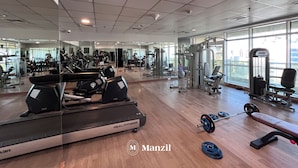 A gym with treadmills, weight machines, and a mirror reflecting the space. - Manzil-1BR near JBR Beach & Blue Waters  (Dubai)