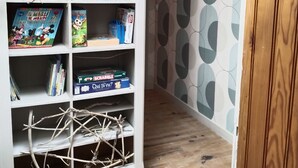 Un corridoio con una libreria bianca piena di libri e giochi, una struttura decorativa a forma di ramo e un muro decorato.