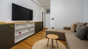 A modern living room with a flat-screen TV, wooden flooring, a sofa, and a small round table. - Room in Porec by Old Town & Waterfront (Porec)