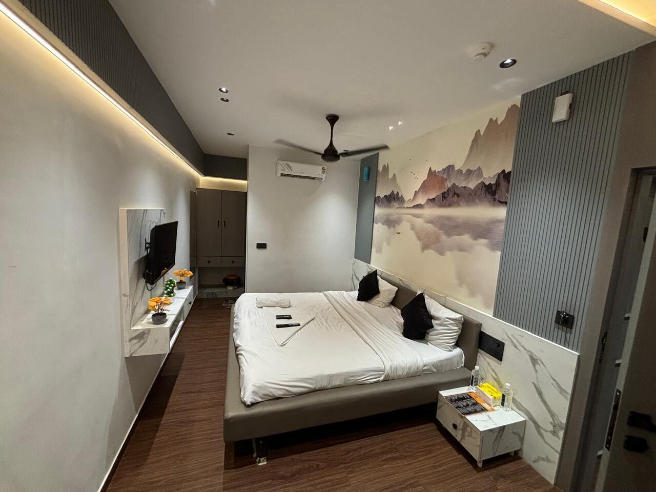 Una habitación de hotel moderna con una cama grande, un televisor, un escritorio y un aire acondicionado instalado en la pared.