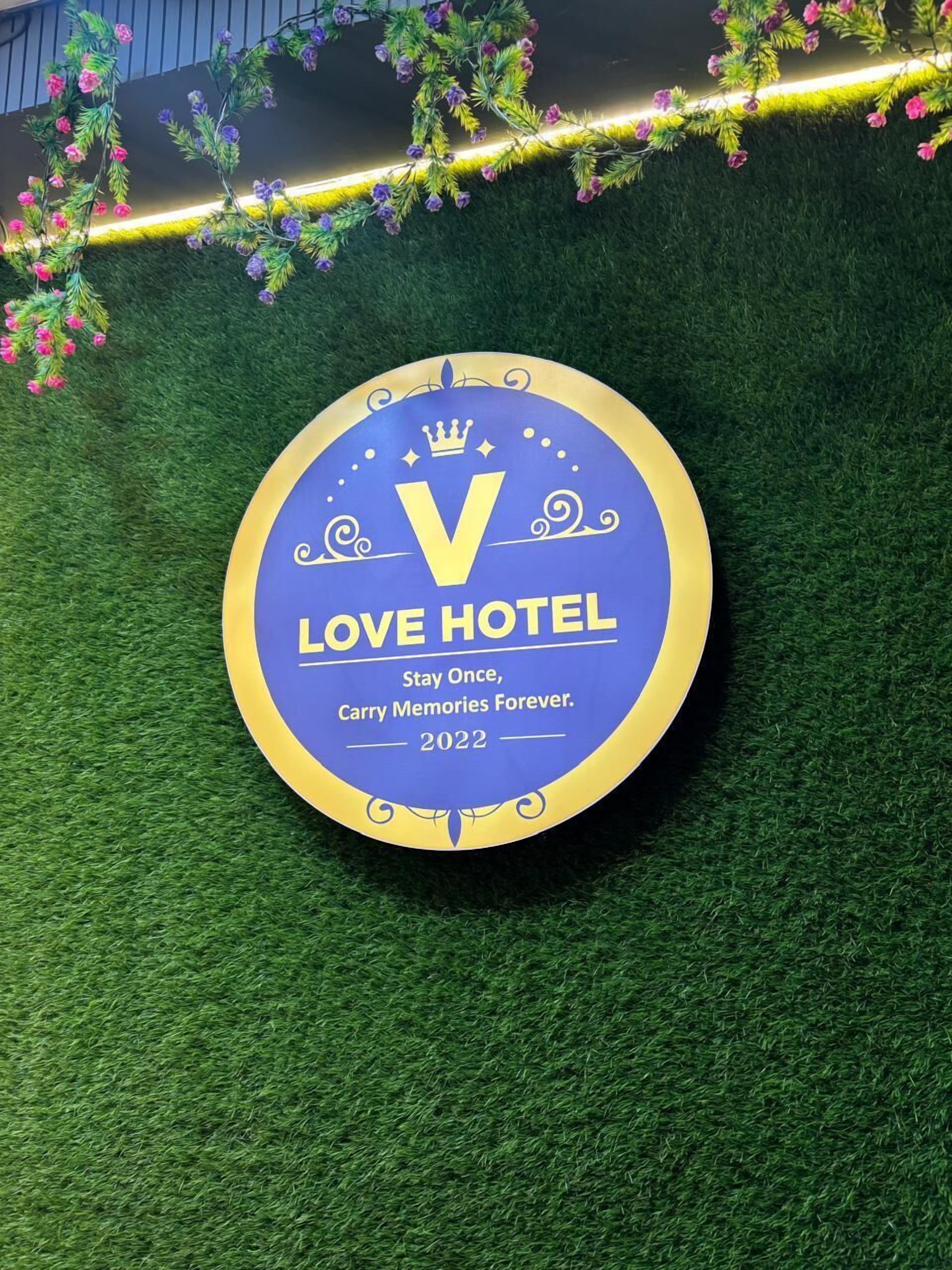Un panneau circulaire avec l’inscription « LOVE HOTEL » et le slogan « Séjournez une fois, emportez des souvenirs pour toujours. 2022 », le tout sur un fond bleu avec une bordure dorée.