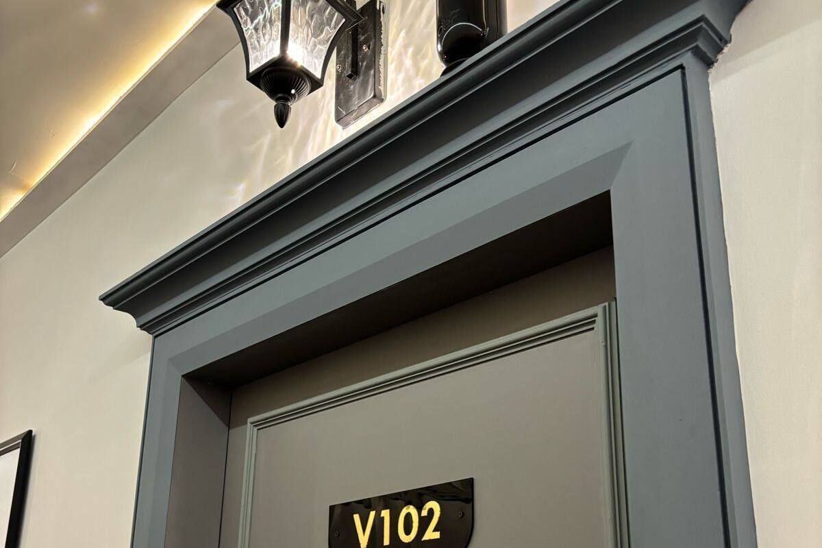 Une porte avec une plaque indiquant « V102 » et un petit luminaire moderne placé juste au-dessus.