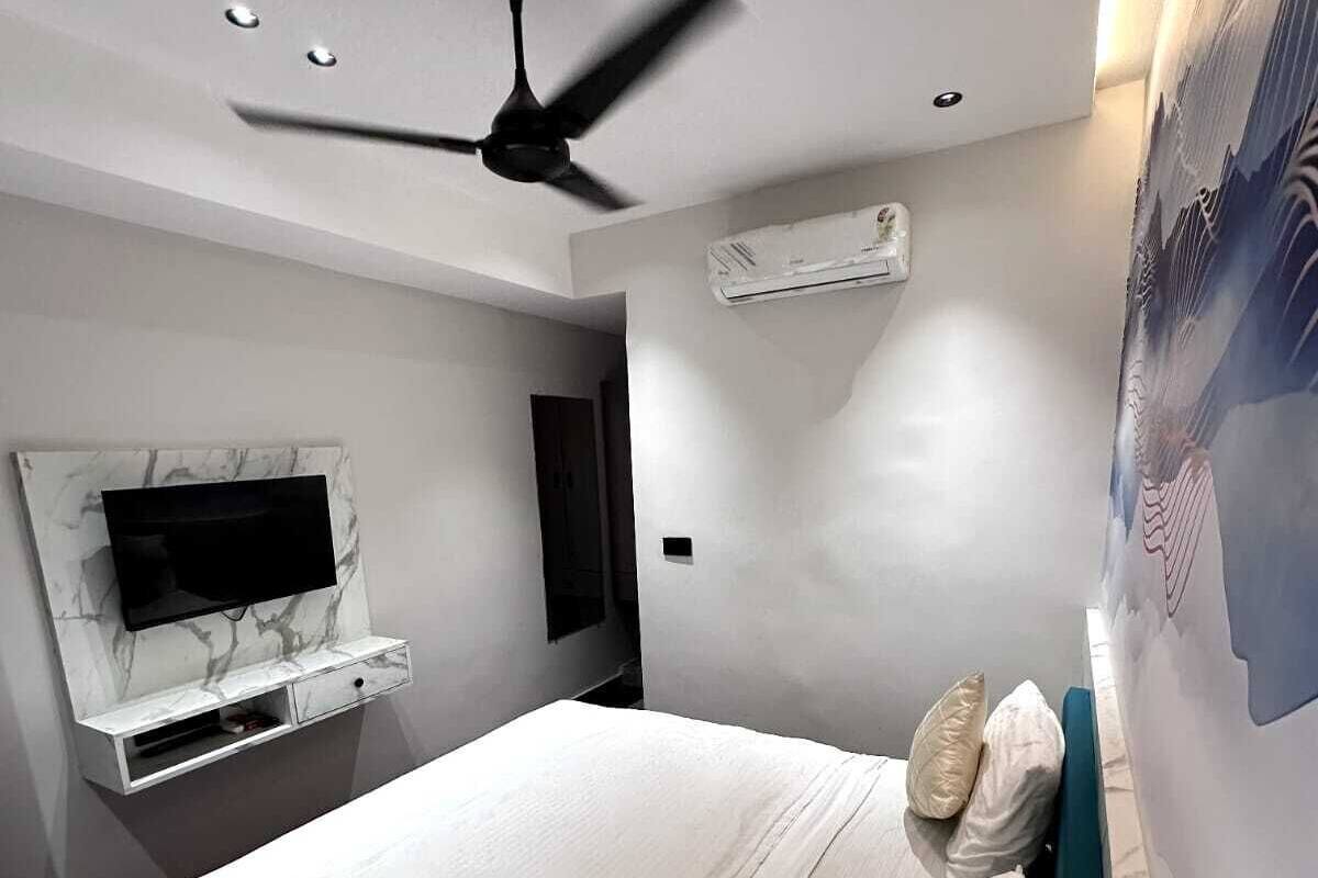 Une chambre moderne dotée d’un grand lit, d’un ventilateur de plafond, d’un téléviseur fixé au mur et d’un appareil de climatisation.