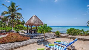 A beachside resort with a thatched-roof gazebo, palm trees, and lounge chairs with towels. - Timeless Oceanfront Villa with Pool in North Akumal (Akumal)