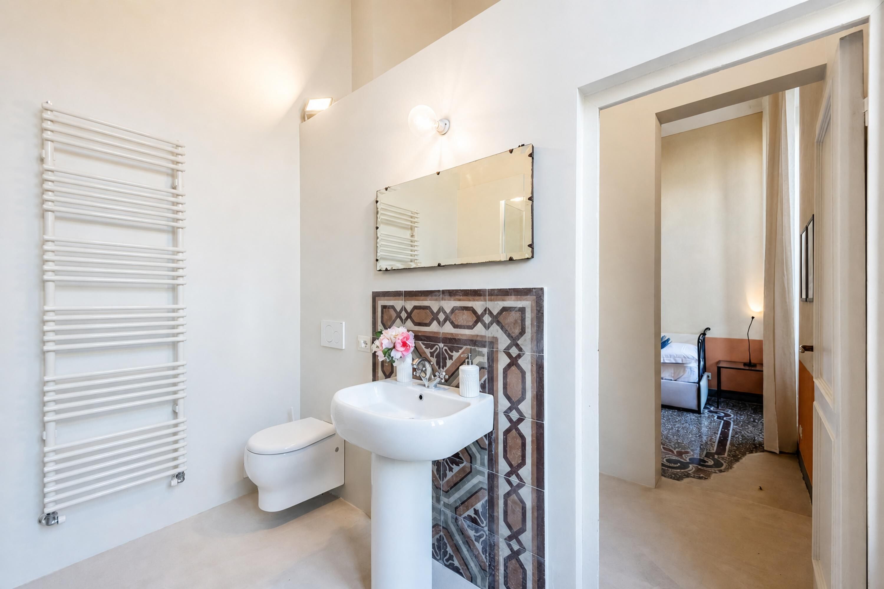 A modern bathroom with a white radiator, a white sink, a mirror, and a patterned tile backsplash.