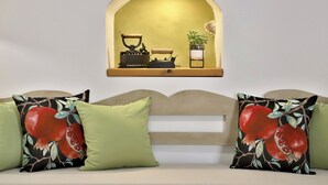 A cozy living room with a sofa adorned with green cushions and a decorative pillow featuring a pomegranate design.