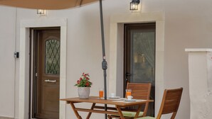 An outdoor seating area with a table and chairs under a large umbrella, a potted plant, and a door with a window.