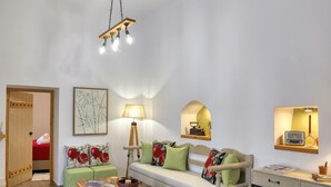 A cozy living room with a wooden floor, a green sofa with red cushions, a wooden coffee table, and a desk with a chair.