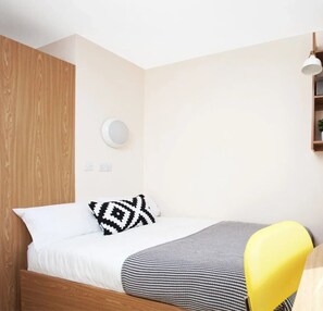 Cozy retreat with a single bed, wall-mounted light, and a small shelf for a personal touch.
