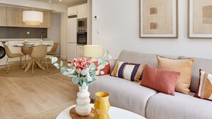 A modern living room with a sofa, a dining table with chairs, and a kitchen in the background. - Zenna | The Rentals Collection (San Sebastián)