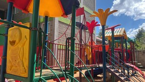 Un'area giochi con strutture colorate, tra cui scivoli e zone per arrampicarsi, con sullo sfondo un edificio con facciata in mattoni.