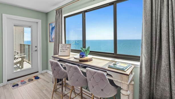 Une pièce dotée d’une grande fenêtre donnant sur la mer, d’un bureau avec des chaises et d’une vue sur le balcon.