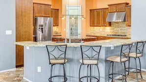 A kitchen with a central island, bar stools, wooden cabinets, a stainless steel refrigerator, and a stone backsplash. - Backyard Oasis w/ Fire Pit: Laveen Village Retreat (Laveen)