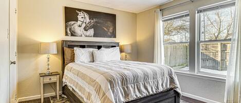 A bedroom with a bed, two bedside tables, a ceiling fan, a large window, and a wall-mounted picture of a horse.