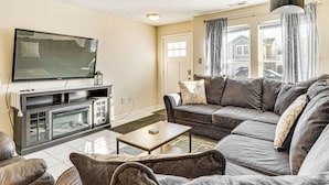 A living room with a large flat-screen TV, a dark-colored sofa, a wooden coffee table, and a fireplace. - 5 Mi to Eagle Creek Park: Home w/ Fenced Yard! (Indianapolis)