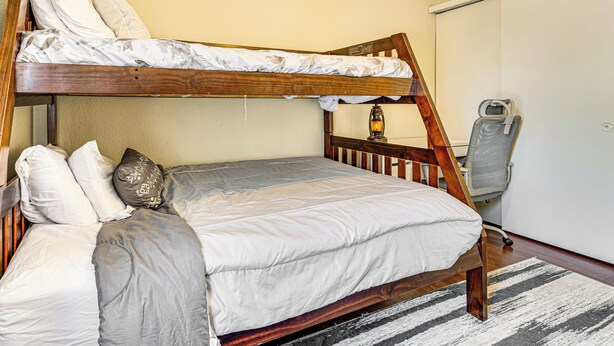 Una cama litera con estructura de madera, ropa de cama blanca y una alfombra a rayas.