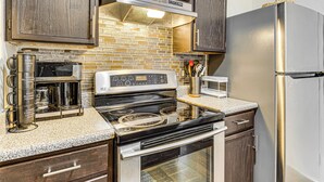 A kitchen with a stainless steel stove, microwave, and refrigerator, wooden cabinets, and a brick backsplash. - 5 Mi to Eagle Creek Park: Home w/ Fenced Yard! (Indianapolis)