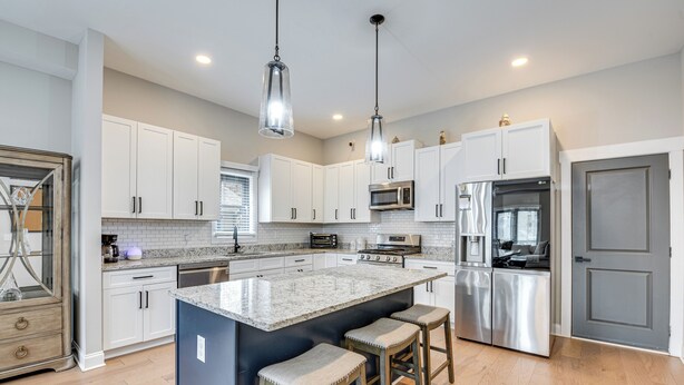 A modern kitchen with white cabinets, stainless steel appliances, and a central island with bar stools. - 3 Mi to Mercedes-benz: Home w/ Office & Backyard! (Atlanta)