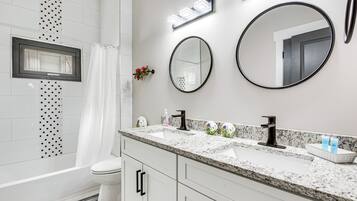 A modern bathroom with a white vanity, two sinks, a toilet, and a shower area.