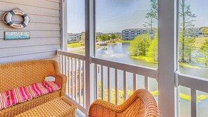 A wicker sofa with a striped cushion on a porch overlooking a river and buildings.