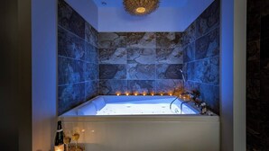 Casa de banho moderna com uma banheira grande, azulejos de parede de pedra e um candeeiro de teto exclusivo.