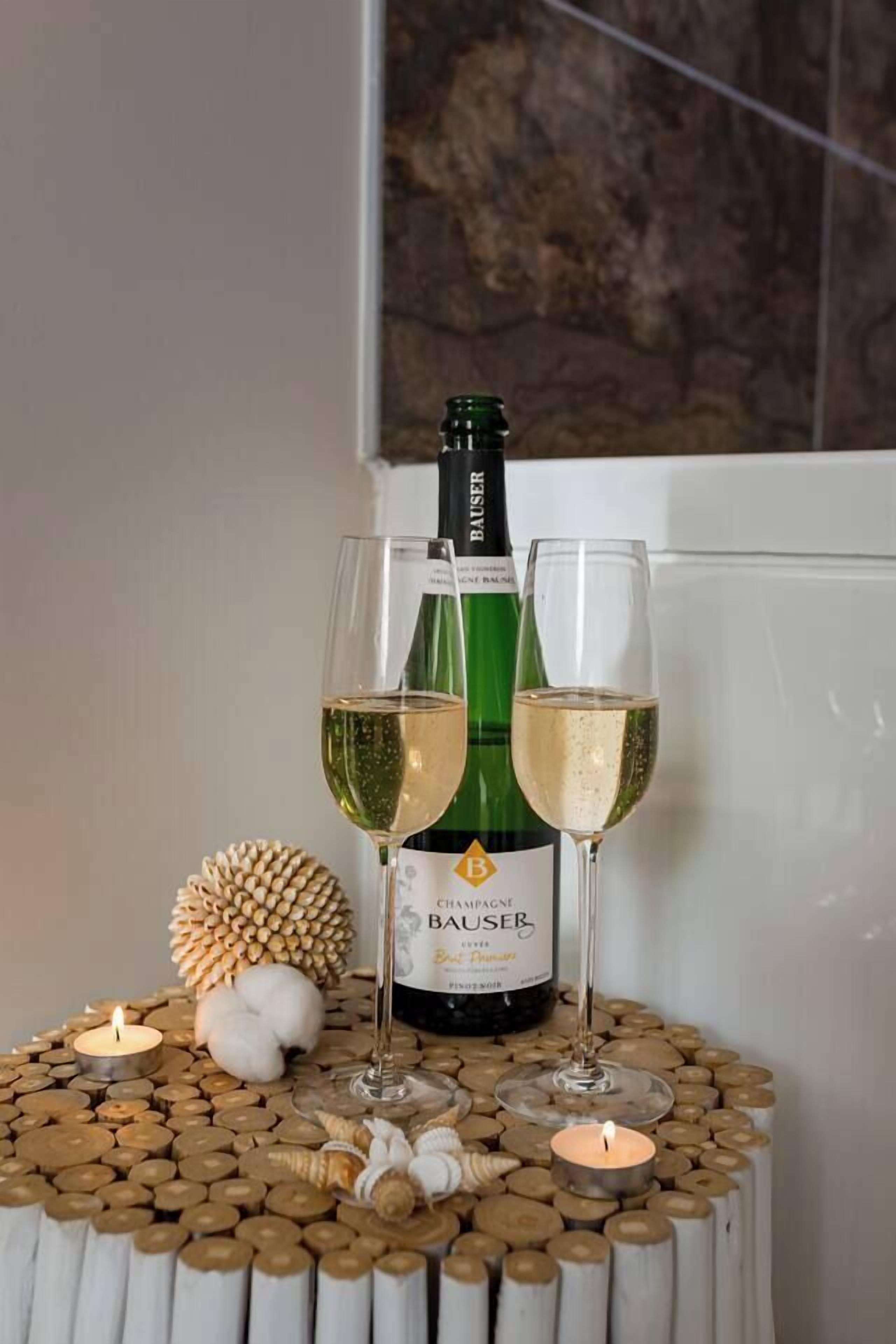 A bottle of champagne and two glasses on a decorative table with candles and seashells.