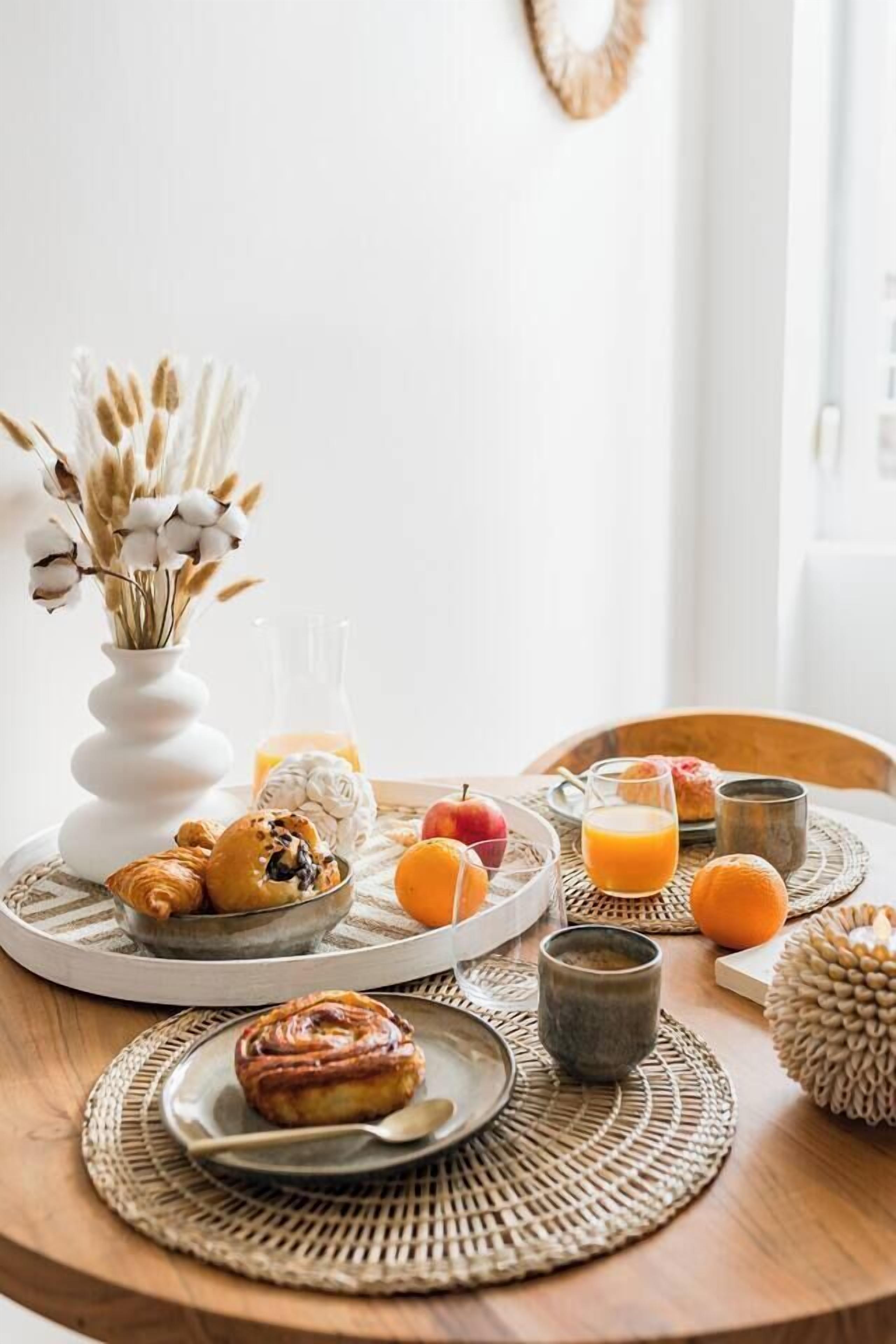 A breakfast setting with croissants, a muffin, oranges, and a glass of orange juice on a wooden table.