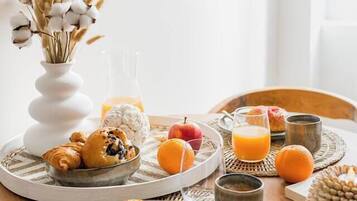 A breakfast setting with croissants, a muffin, oranges, and a glass of orange juice on a wooden table.