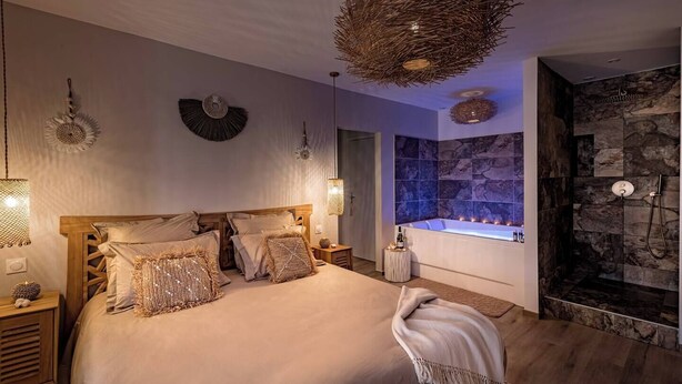 Um quarto espaçoso com uma cama grande, uma banheira de pedra e área de chuveiro.