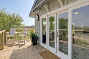 A deck with two white chairs, a potted plant, and a glass door leading to a patio area.