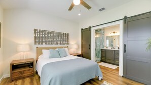 A bedroom with a bed, nightstands, a ceiling fan, a wall art piece, a sliding door leading to a bathroom, and a kitchen area. - 3 Mi to Rockport Beach: Home Near Aransas Bay (Rockport)
