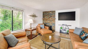 A modern living room with leather sofas, a round coffee table, a fireplace, and a large flat-screen TV mounted on the wall. - Walk to Beaches: Waterfront Home in Port Orchard! (Port Orchard)