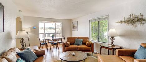 A spacious living room with a brown leather sofa, a round coffee table, and a dining area with wooden chairs and a table.