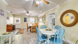 Un'area pranzo con un tavolo rotondo e sedie blu, una ventola a soffitto e uno specchio decorativo appeso al muro.