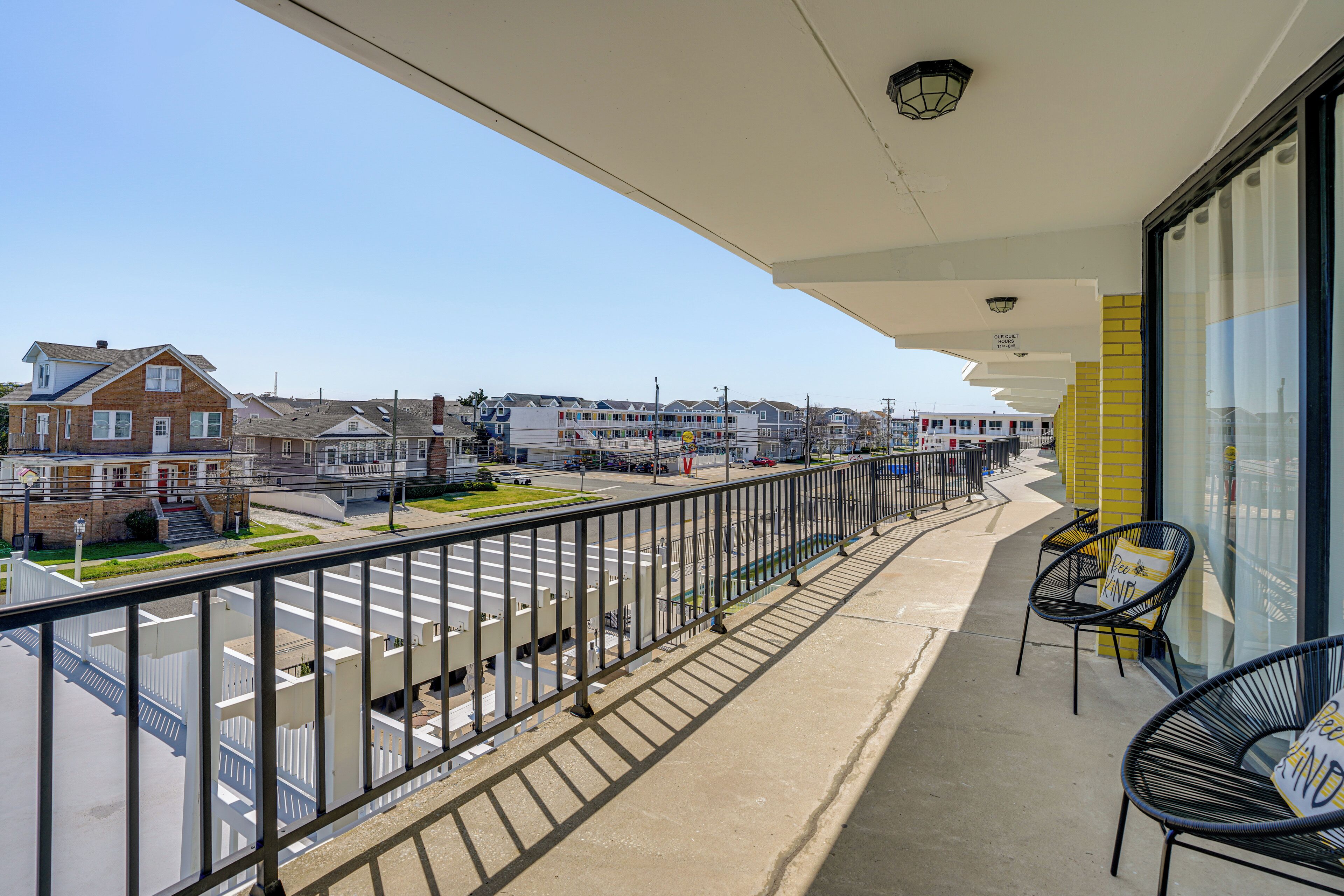 Een balkon met uitzicht op een straat en huizen, met een hekwerk, stoelen en een bord.
