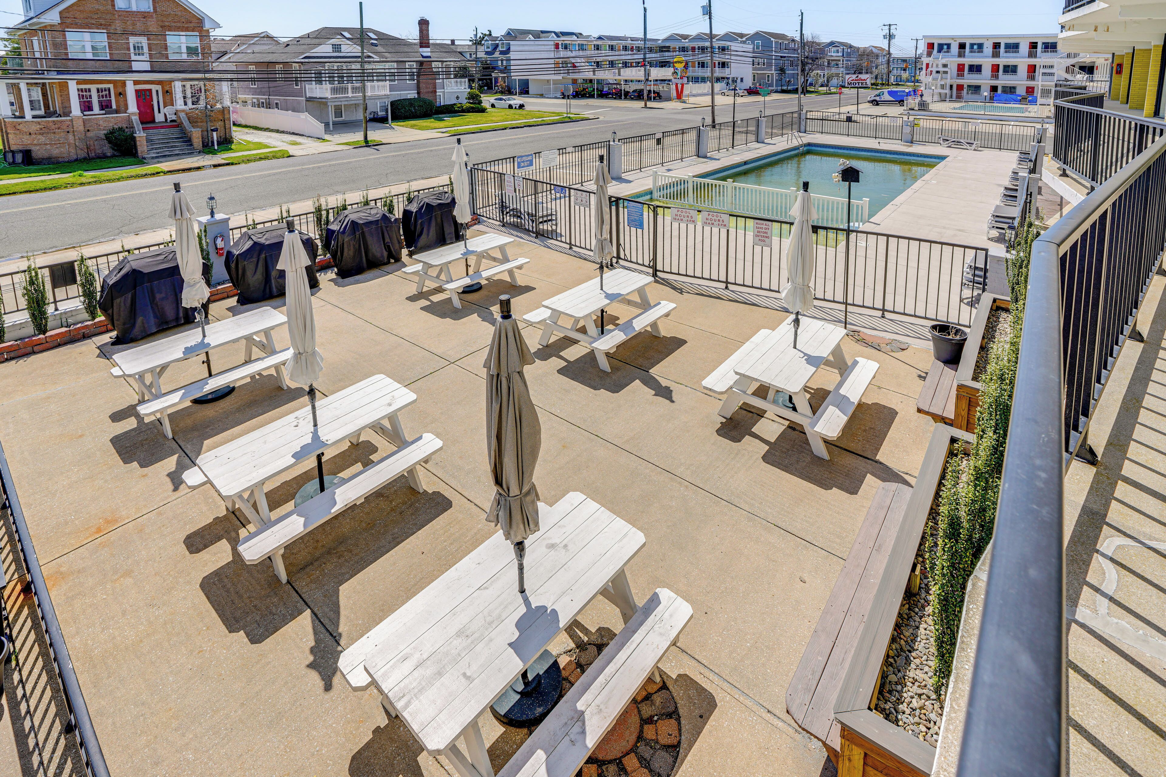 A rooftop patio with picnic tables and umbrellas, a swimming pool, and a view of the surrounding neighborhood.