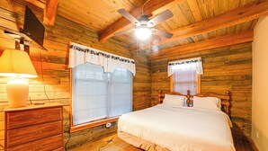 Camera da letto in una baita di legno con un letto, una cassettiera e una ventola a soffitto.