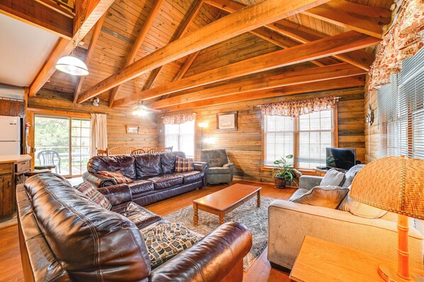 A cozy log cabin interior with a leather sofa, a wooden coffee table, and a television in the living area. - Game Room & Decks: Family Cabin in Springville! (Springville)