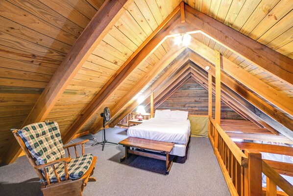 A cozy attic bedroom with a wooden ceiling, a bed, a chair, and a small table. - Game Room & Decks: Family Cabin in Springville! (Springville)