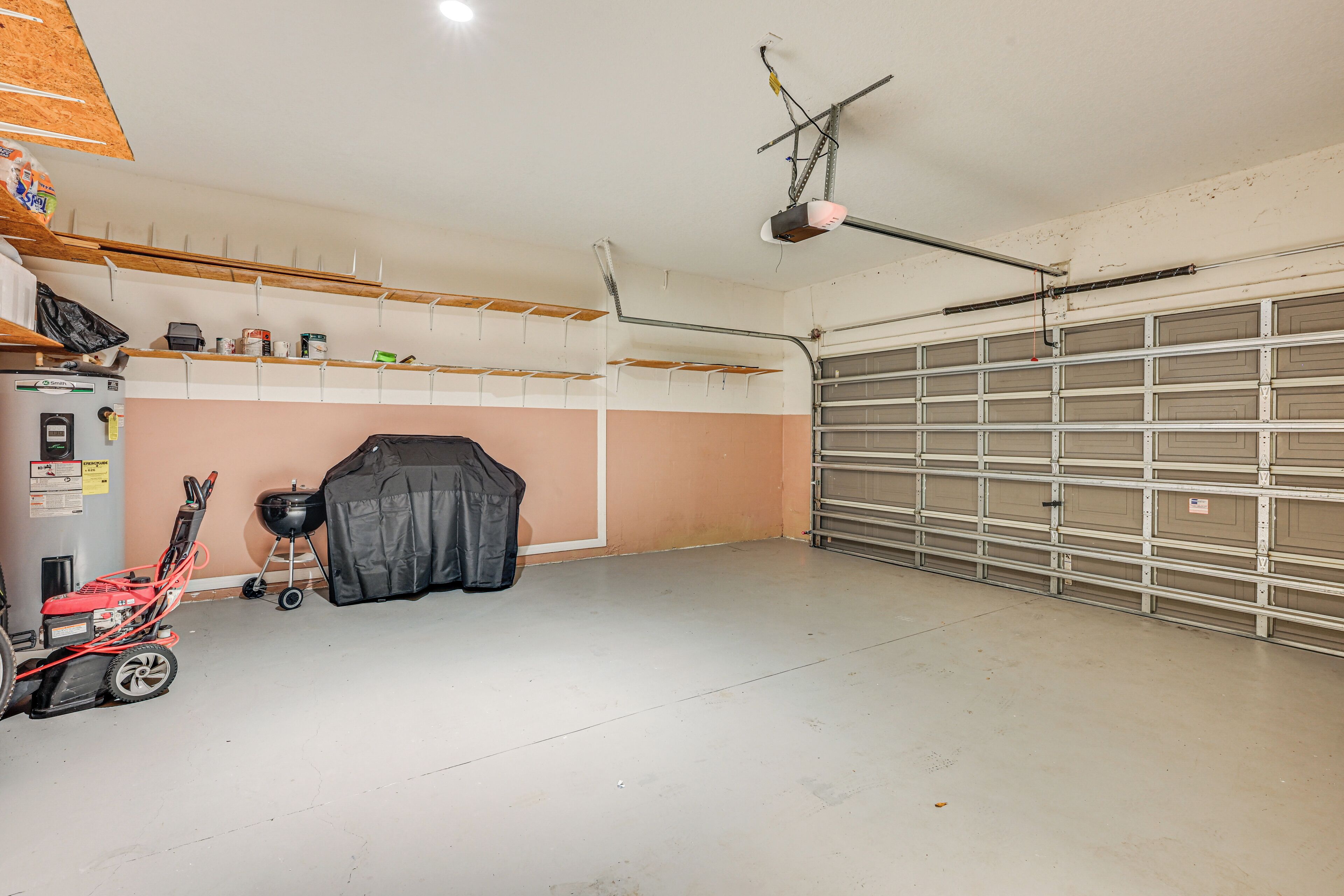 Garagem com piso de concreto, ventilador de teto, cortador de grama vermelho, churrasqueira coberta e porta de garagem.
