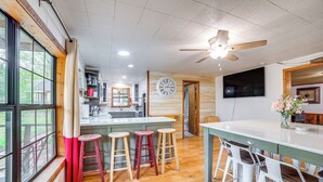 A kitchen with wooden cabinets, a central island with stools, a ceiling fan, and a large clock on the wall.
