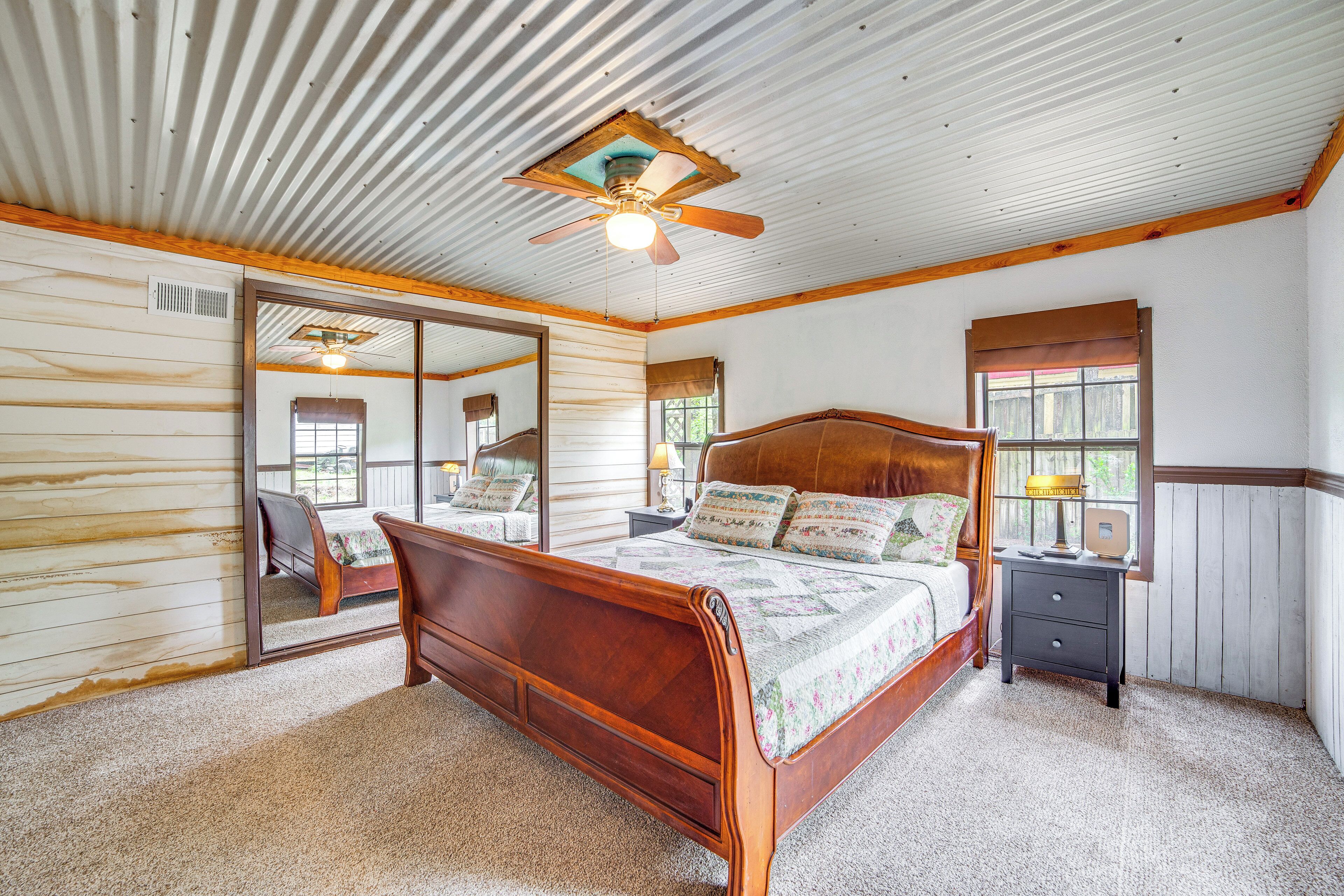 A bedroom with a wooden bed, a nightstand, a mirror, and a ceiling fan.
