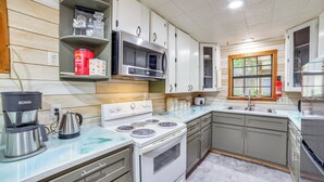 A kitchen with a stove, microwave, and coffee maker. There are cabinets and a window with a view.