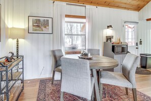 A dining area with a round table, two chairs, a lamp, a framed picture, and a window with a view of trees. - Cozy Cabin + Casita Pinetop Forest Retreat (Pinetop)