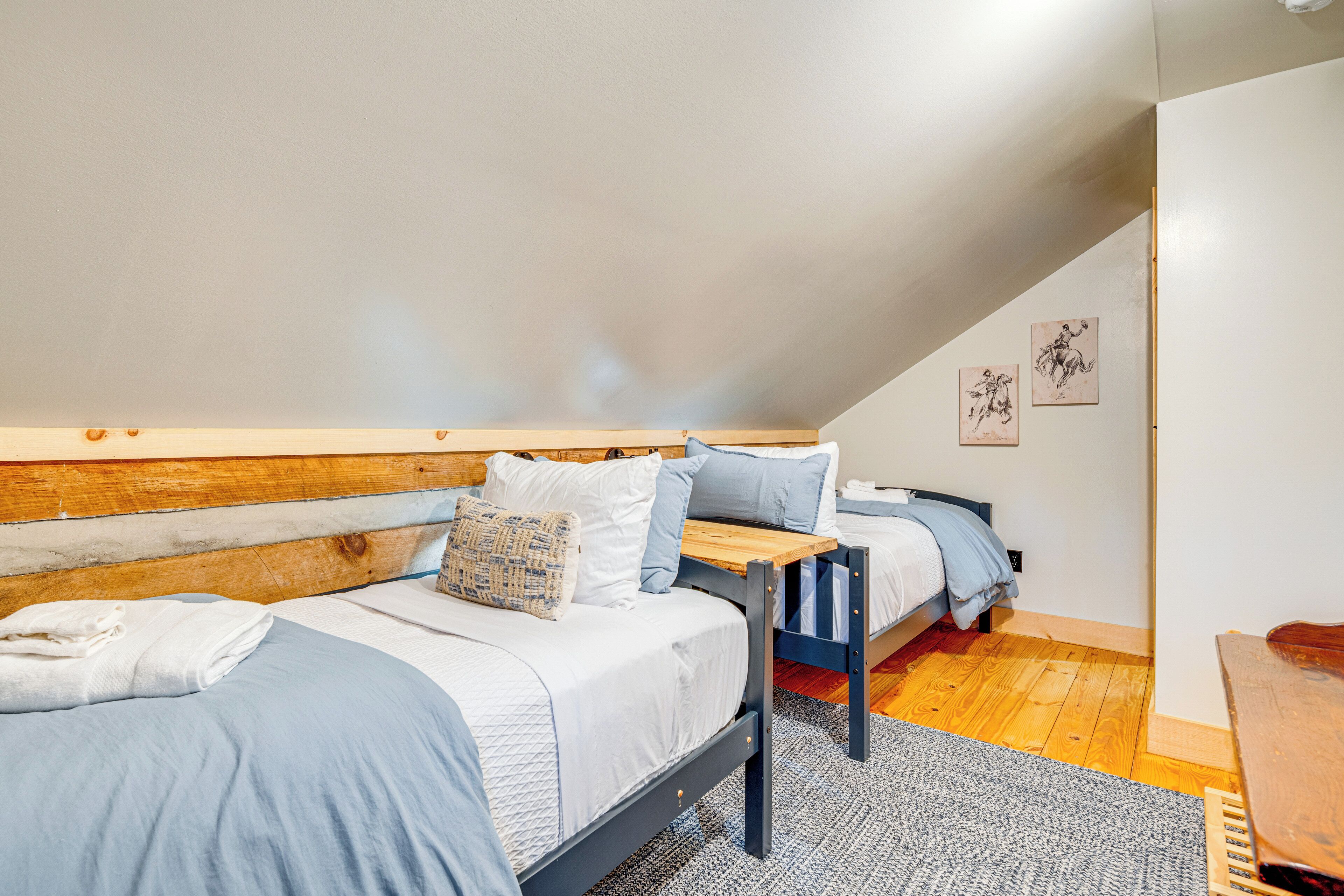 A bedroom with two beds, a wooden headboard, a small table, and a gray rug.
