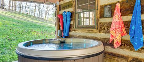 A hot tub in a log cabin with a wooden exterior, a window, and towels hanging on the wall.